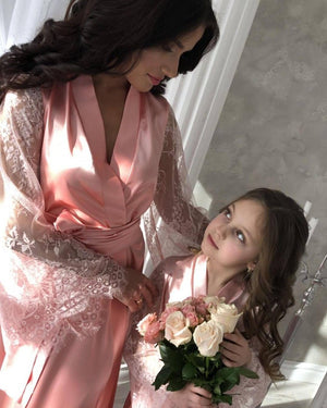 Woman and young girl in matching pink dresses holding flowers indoors.