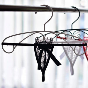 A white micro thong panty with intricate lace detailing, displayed on a wooden surface surrounded by various accessories such as a red candle, a bottle of nail polish, and a photograph.