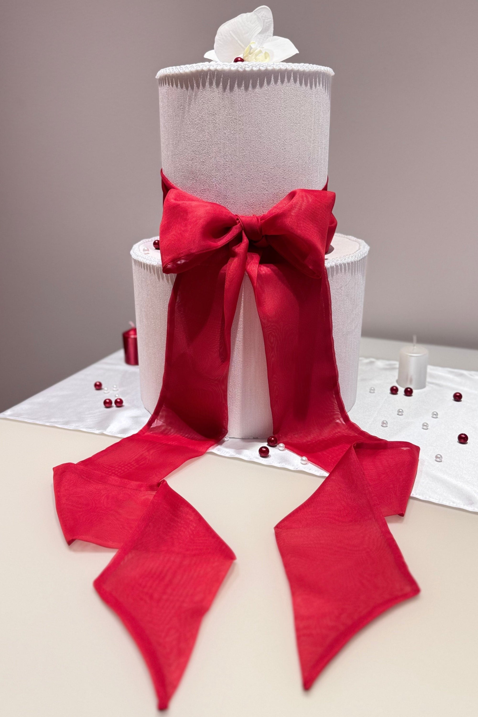 A white wedding cake topped with a red chiffon ribbon bow.