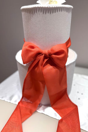 A white wedding cake topped with a red chiffon ribbon bow.