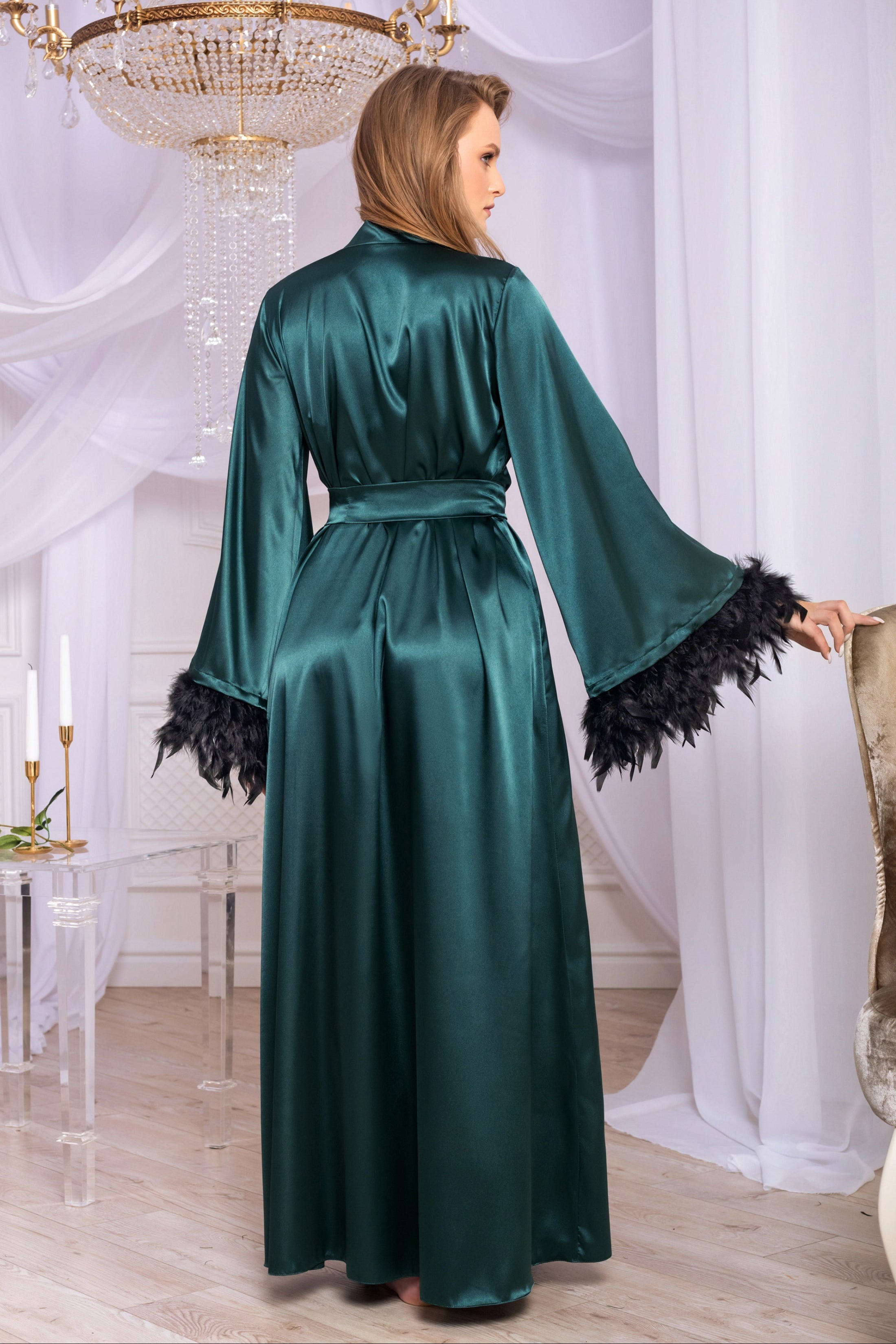 Woman wearing a green satin robe with black feather details in an elegant room.