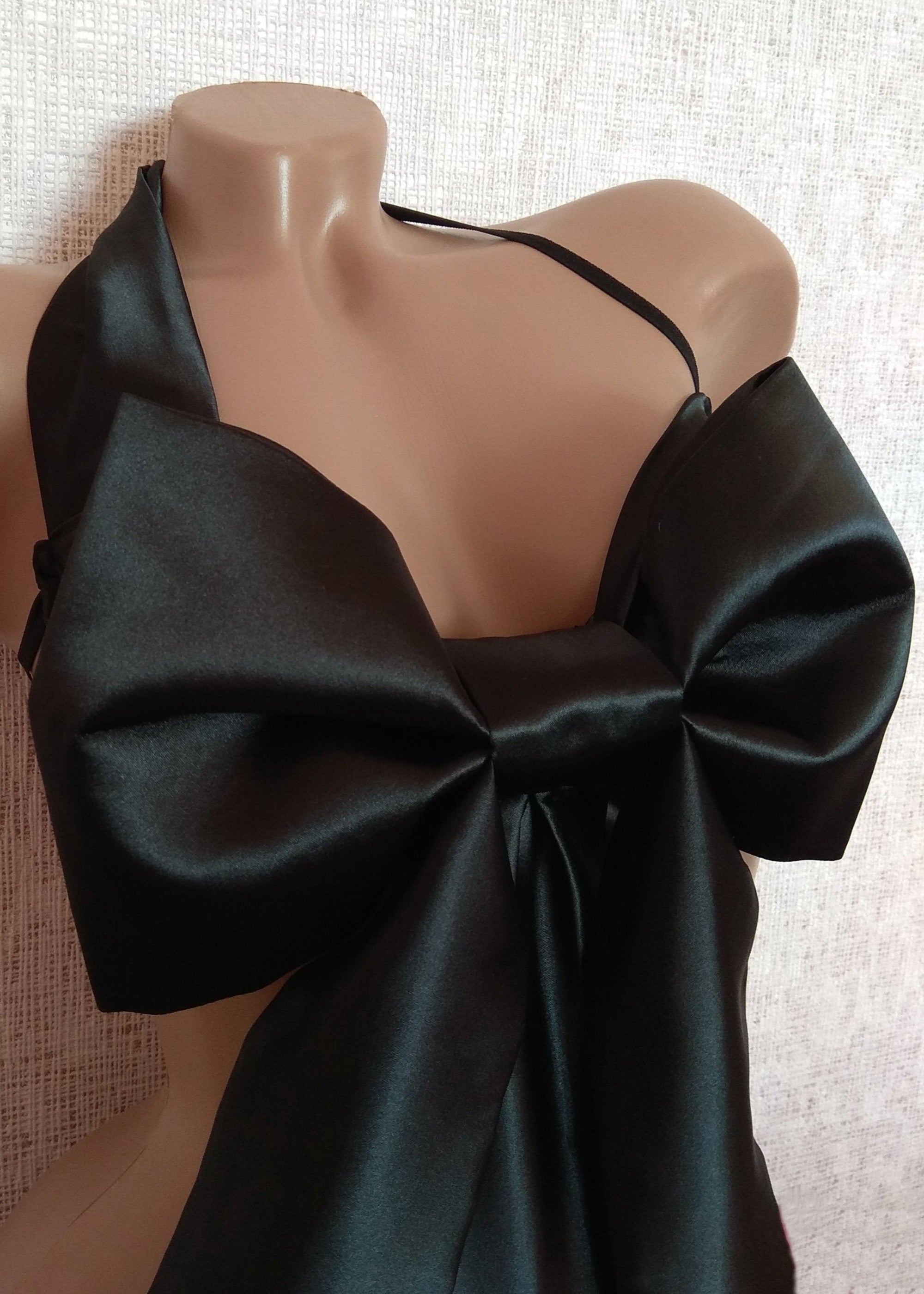 Black satin top with a large bow on a mannequin against a textured white background