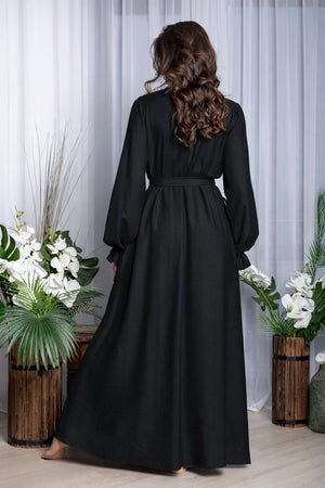 Woman wearing a black dress standing in a room with white curtains and plants.