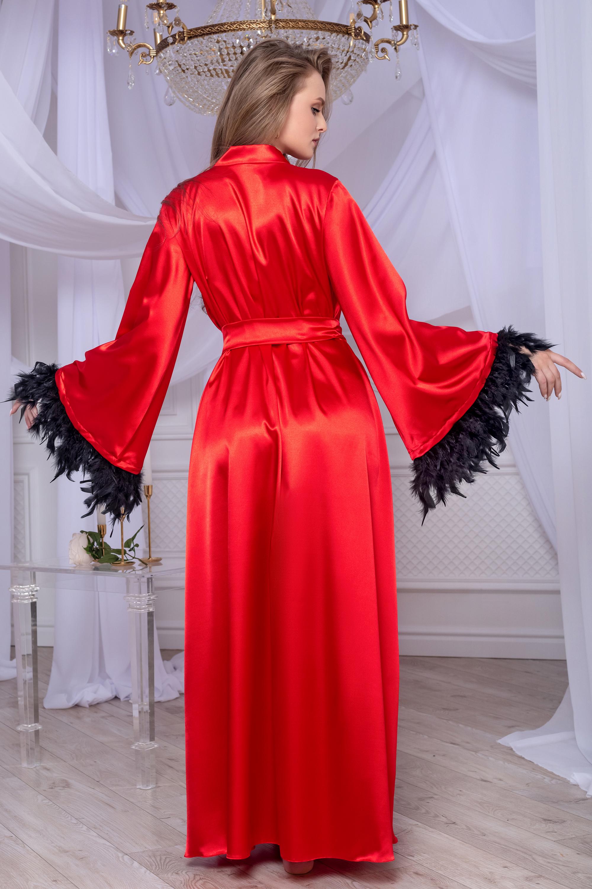 Woman wearing a red satin robe with black feathered cuffs in an elegant room.