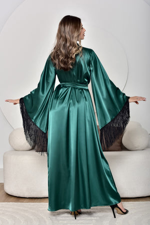 Woman wearing a green satin dress with black fringe details, standing against a white background.