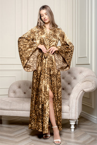 A woman standing in a luxurious room wearing a gold and leopard print kimono-style robe with a wide sash, paired with white sandals.