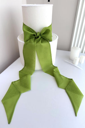 Green ribbon tied in a bow on a white cylindrical object against a neutral background