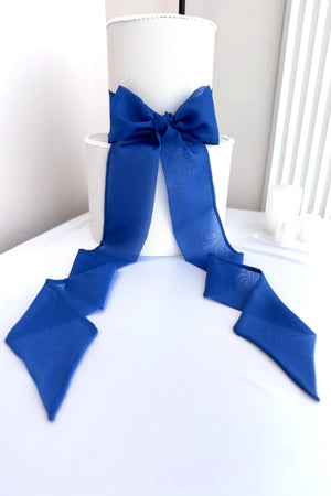 White cake with a large blue bow on a white surface