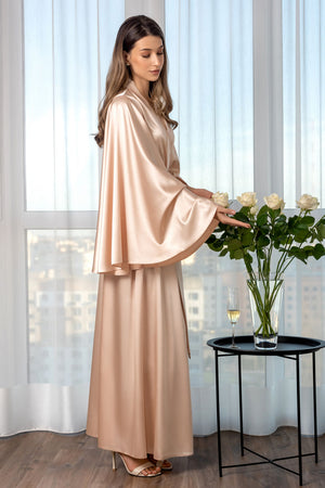 Woman in a beige outfit arranging flowers in a room with large windows.
