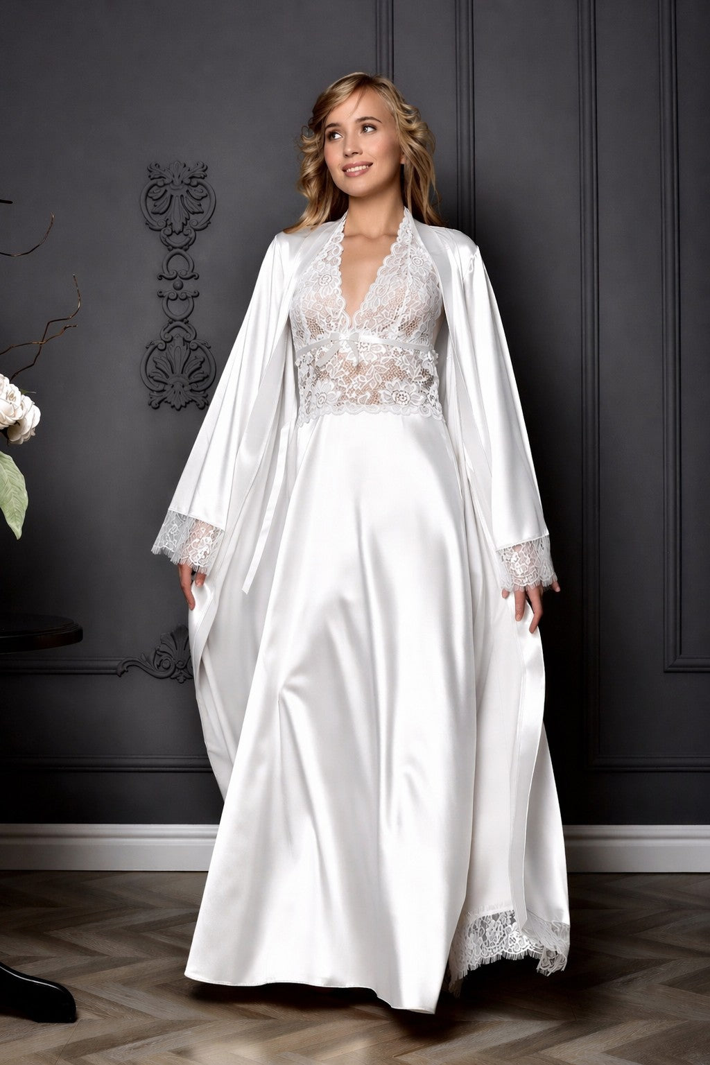 Woman wearing a white lace dress with a matching robe against a dark wall.
