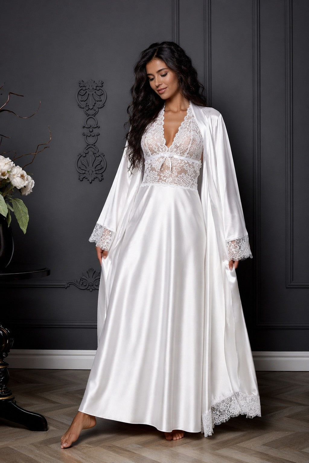 Woman wearing a white lace dress with a matching robe against a dark wall.