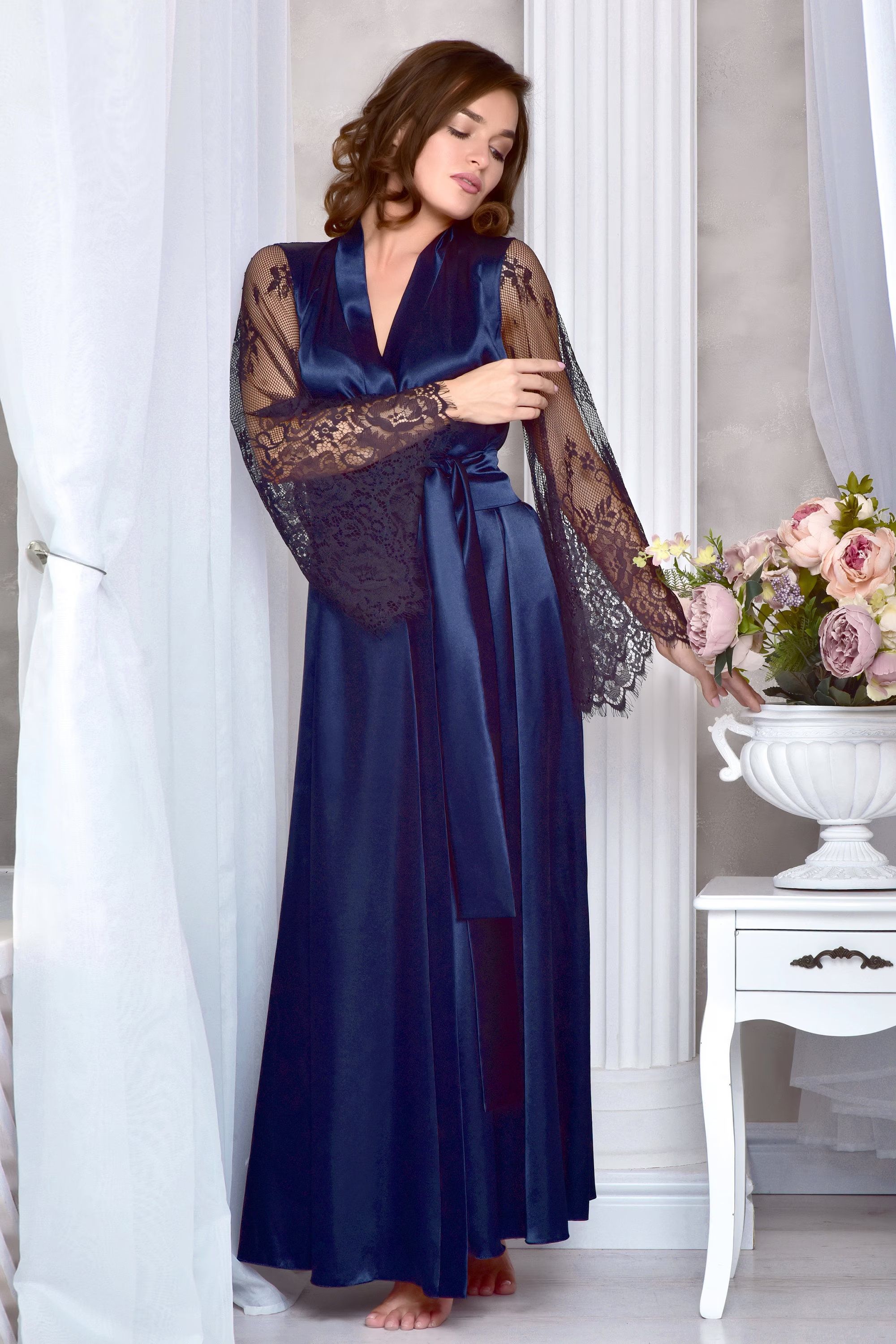Woman wearing a long navy blue satin robe with lace sleeves in a elegant room.