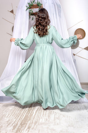 Woman wearing a light green dress with long sleeves in a minimalistic setting.
