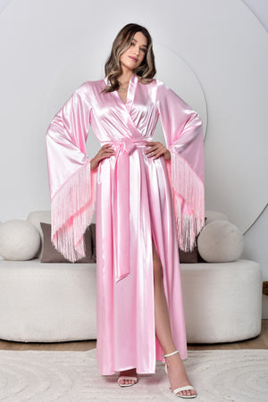 A woman wearing a pink fringe trim long robe with a wide sash, standing in a room with a light background.
