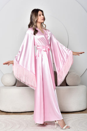 Woman wearing a pink satin robe with fringe details in a minimalistic setting.