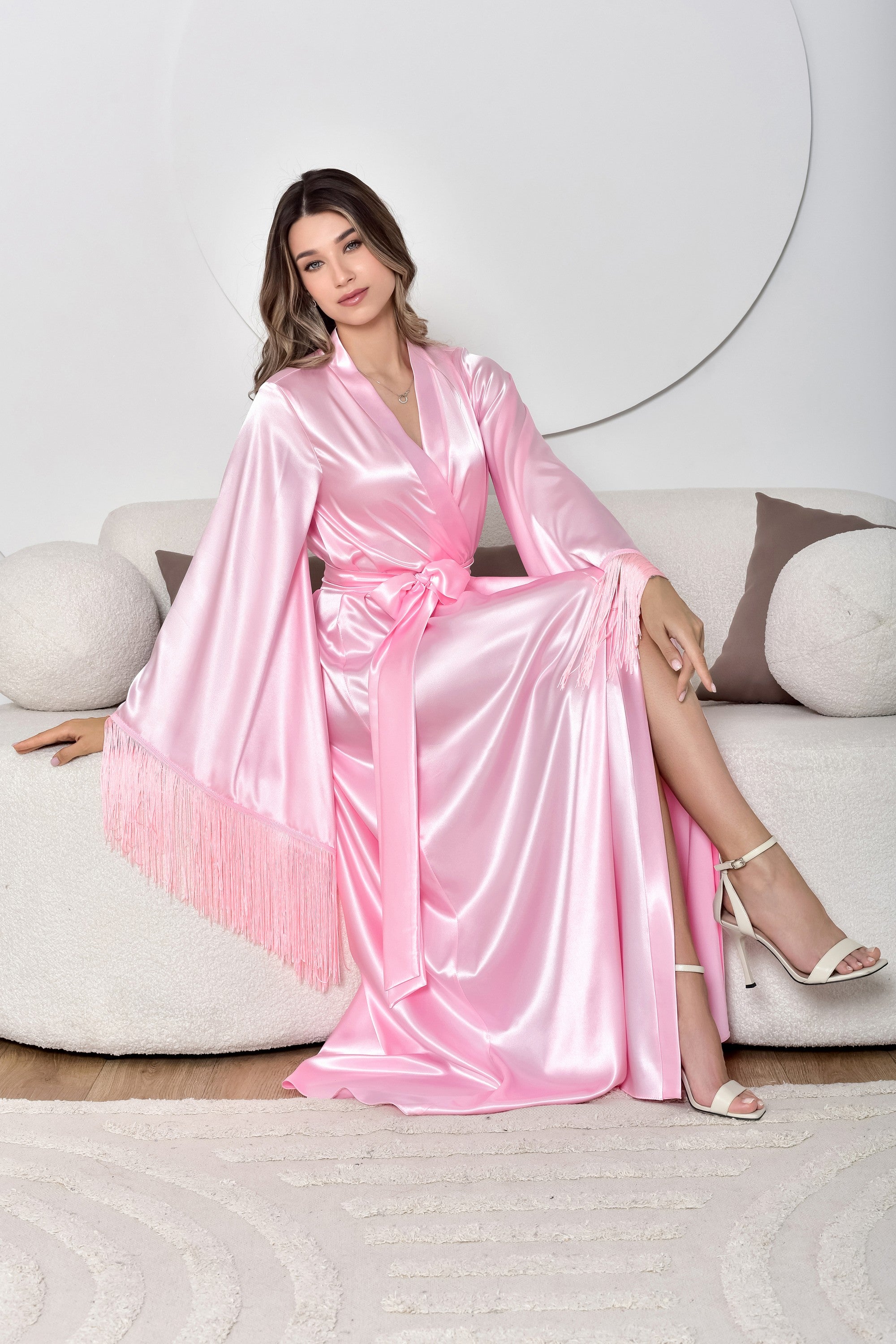 Woman in a pink satin robe sitting on a white couch.