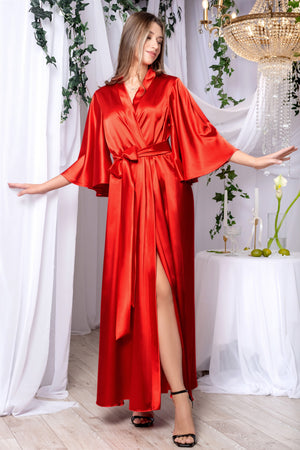 A woman wearing a red satin dressing gown that reaches her floor, with three-quarter sleeves and a tied waist