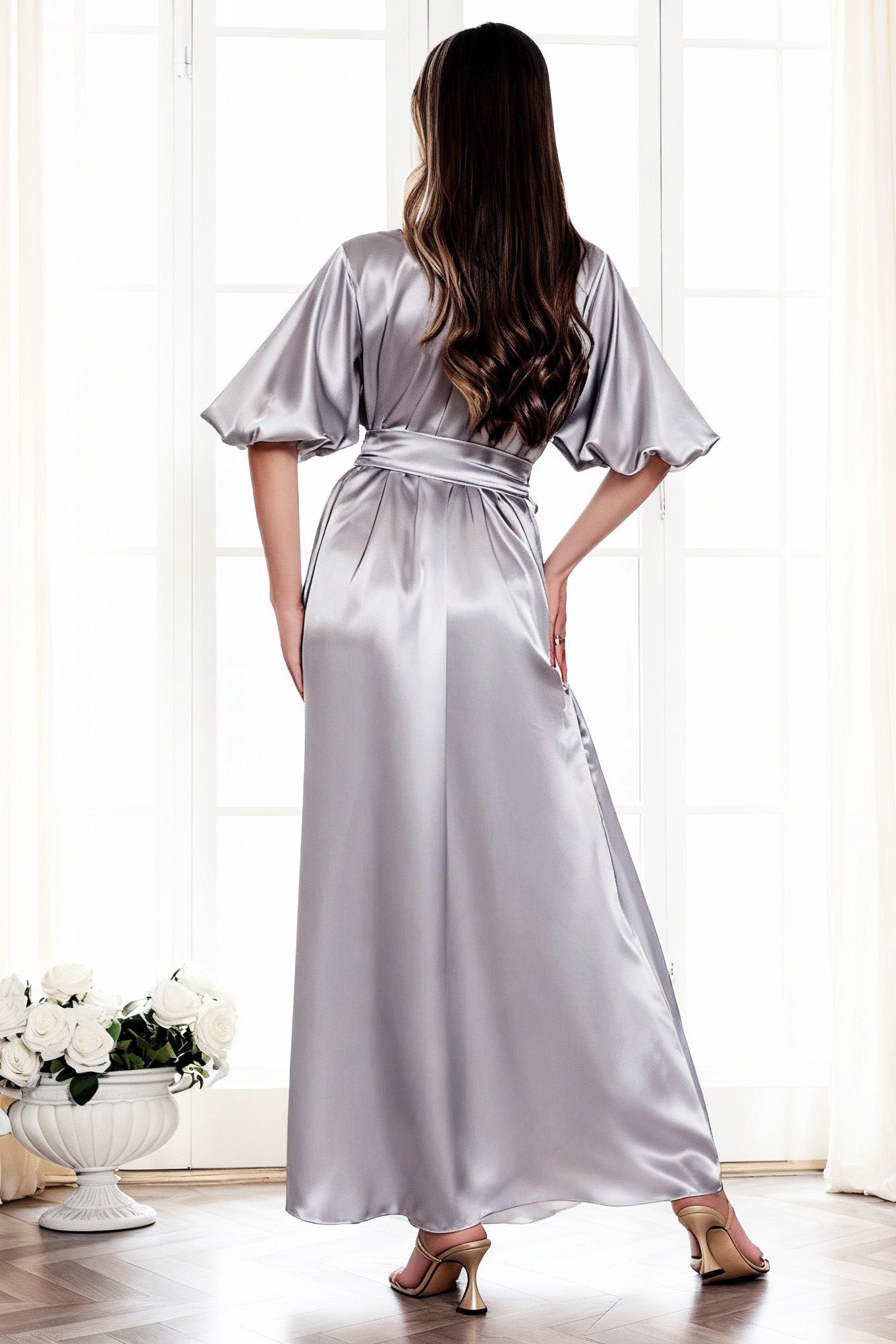 Woman wearing a silver satin robe in a bright room with white curtains.