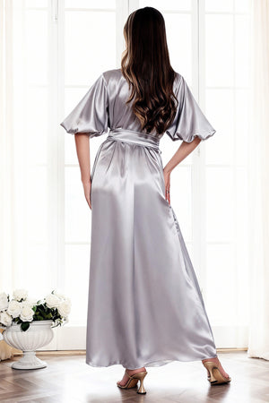 Woman wearing a silver satin robe in a bright room with white curtains.