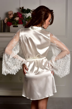 Woman wearing a white satin robe with lace sleeves in a room setting.