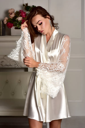 Woman wearing a white satin robe with lace details in a elegant room setting.