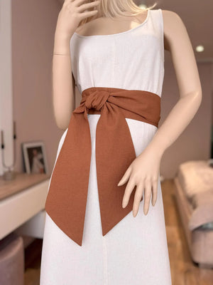 A mannequin wearing a white dress with a pink linen sash tied in the middle.