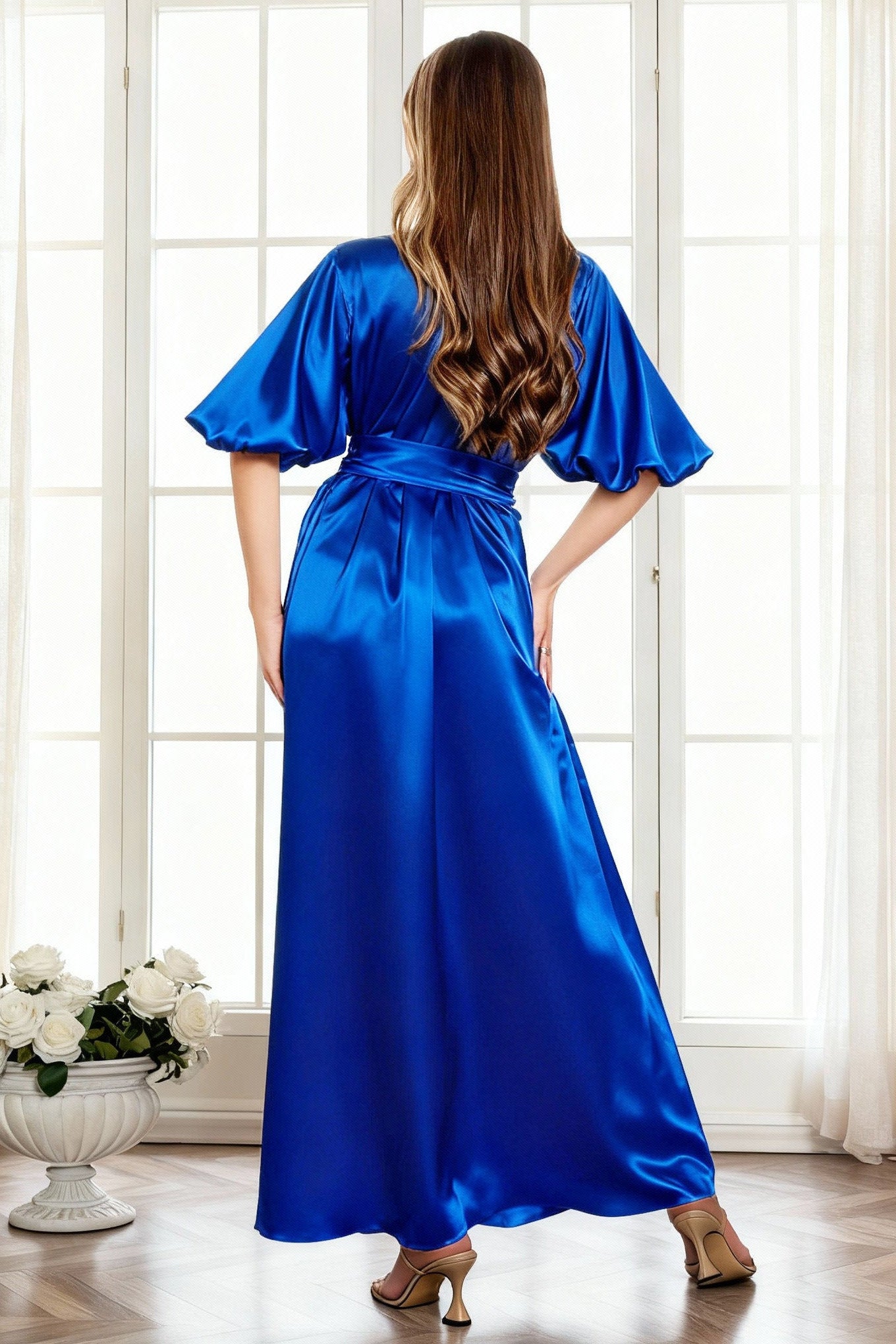Woman wearing a blue satin dress standing in a room with large windows
