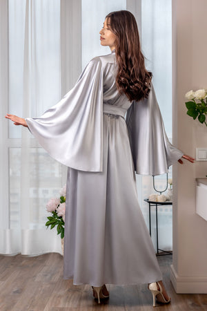 Woman wearing a silver satin robe standing in a well-lit room with white curtains