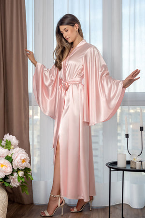 Woman wearing a pink satin robe in a room with curtains and a table with candles