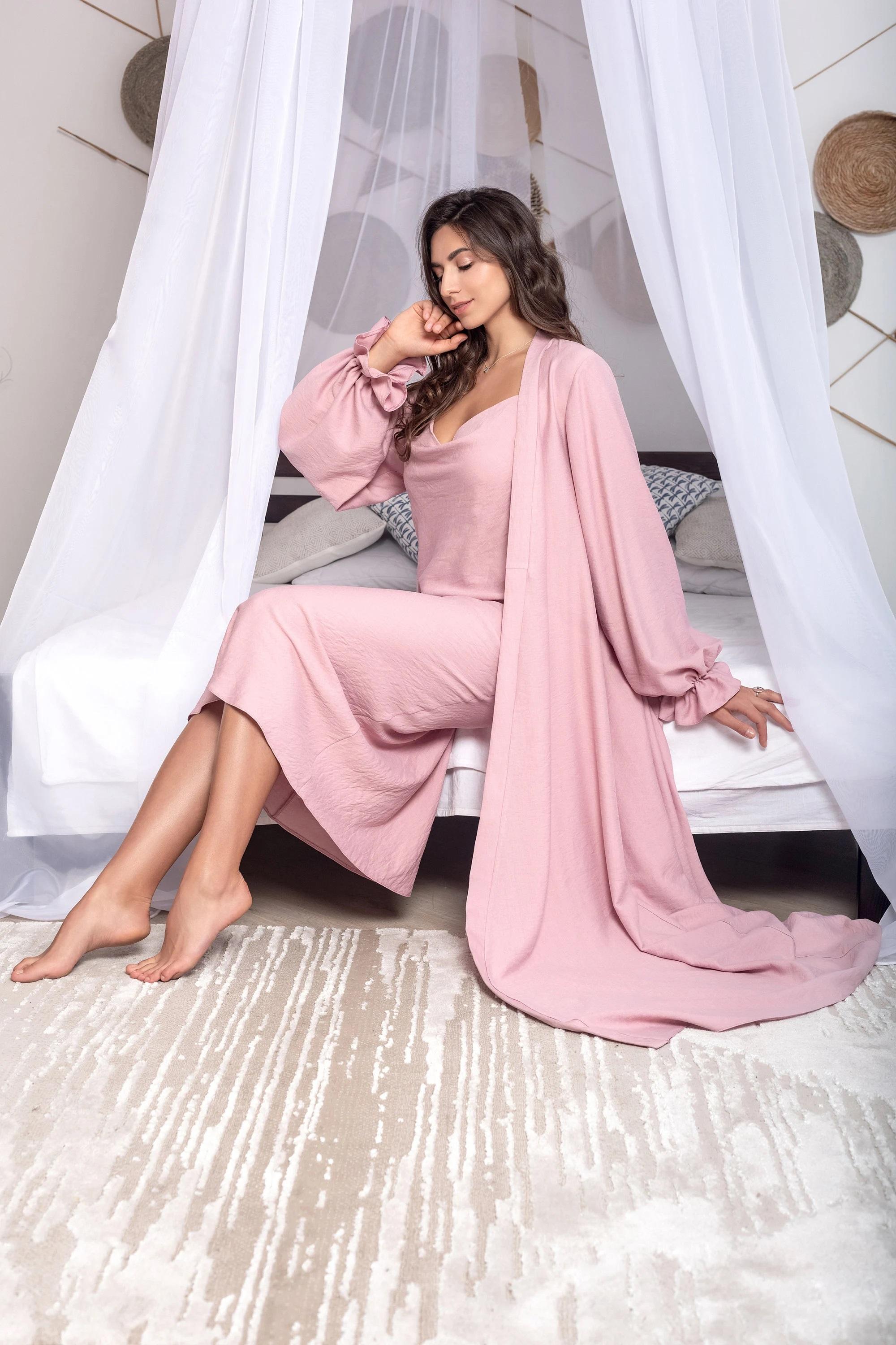 Woman in a pink outfit sitting on a bed with white curtains in the background