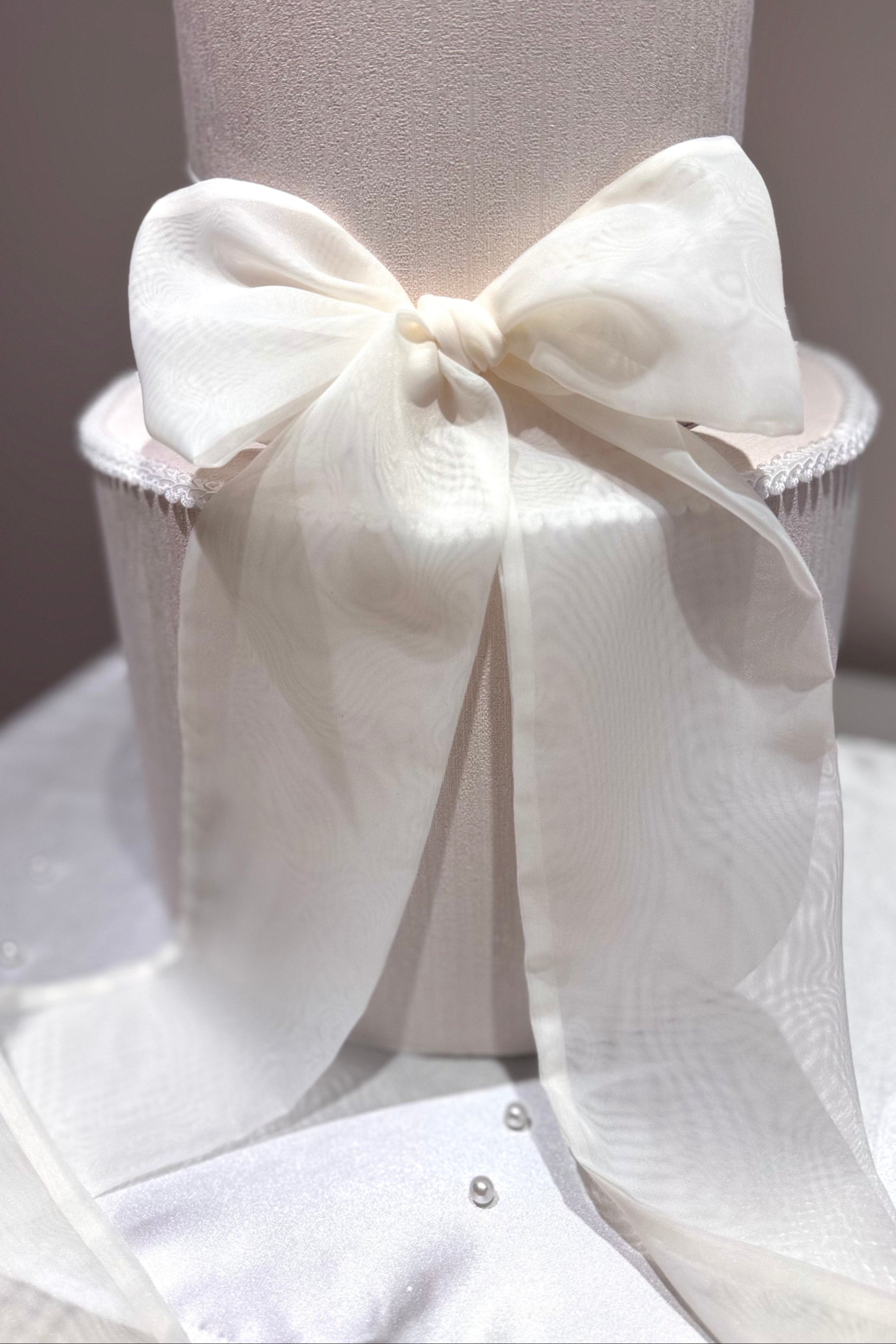 A white wedding cake topped with a red chiffon ribbon bow.
