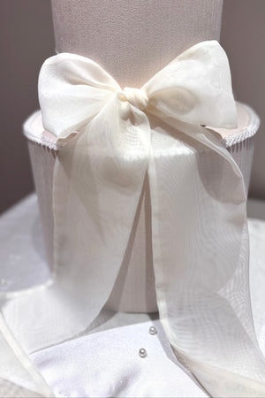 A white wedding cake topped with a red chiffon ribbon bow.