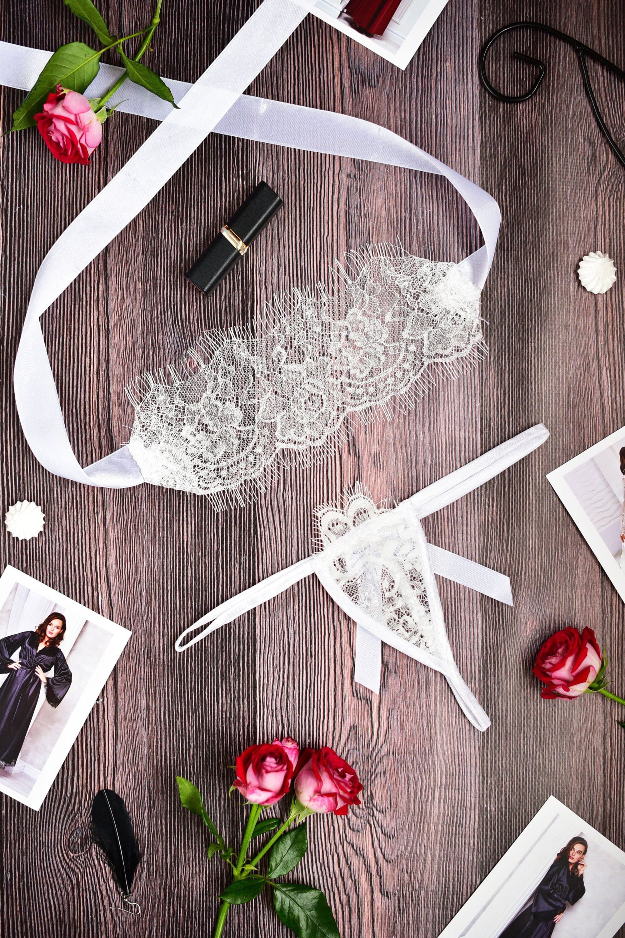 A white lace blindfold and thong panties on a wooden surface, surrounded by decorative items and flowers.