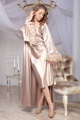 A woman wearing a beige satin robe with feather trim, elegant decor.
