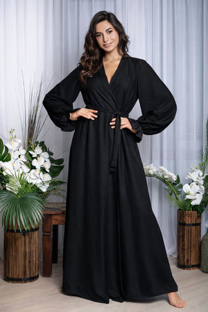 Woman wearing a black dress standing in a decorated room with plants and white curtains.