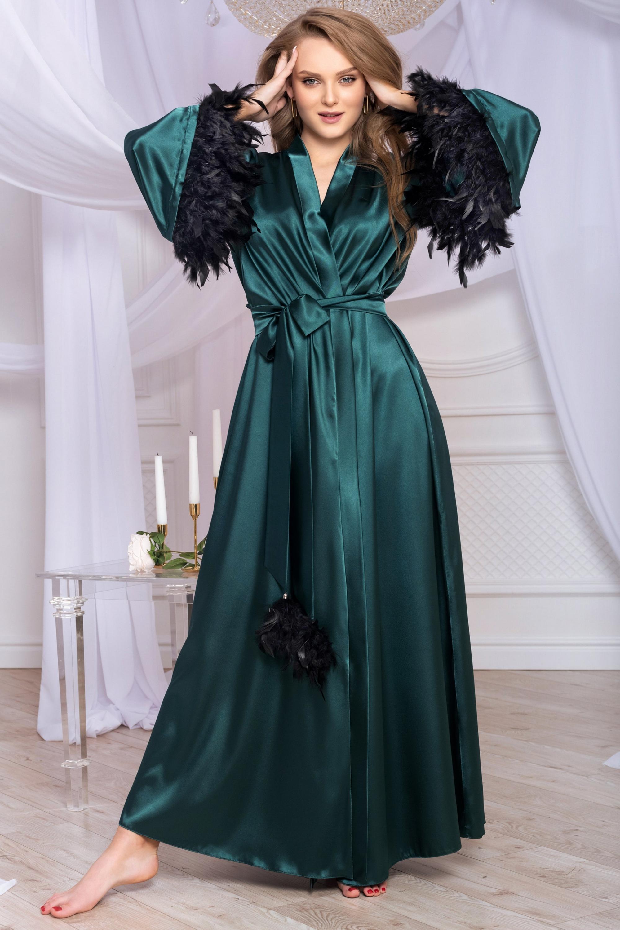 Green satin dress with black feathered sleeves in a decorated room.