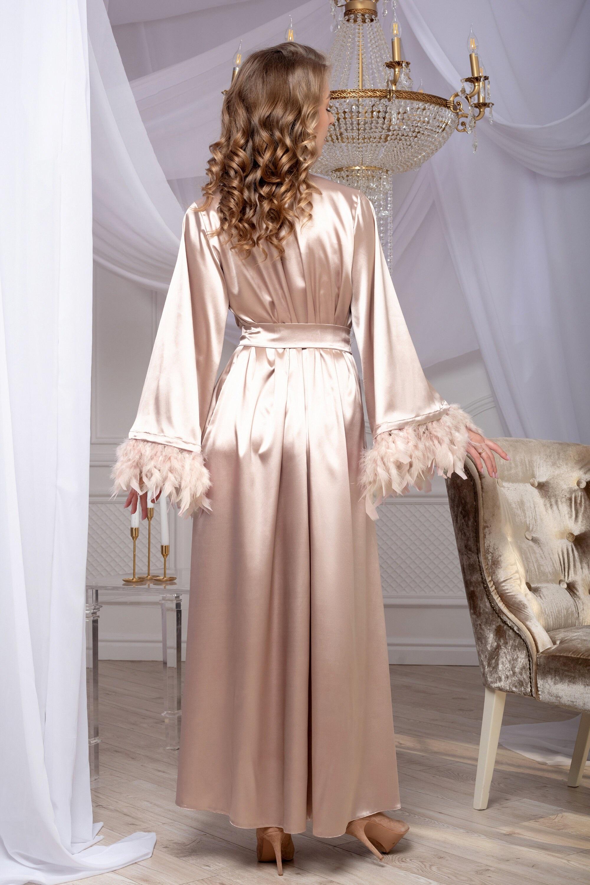 Woman in a long, light-colored dress standing in a room with white curtains and a chandelier.