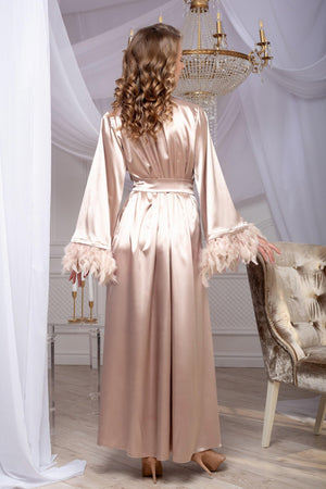 Woman in a long, light-colored dress standing in a room with white curtains and a chandelier.