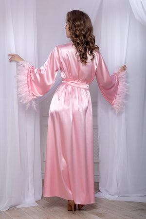 Woman wearing a pink satin robe with frilled cuffs in a room with white curtains.