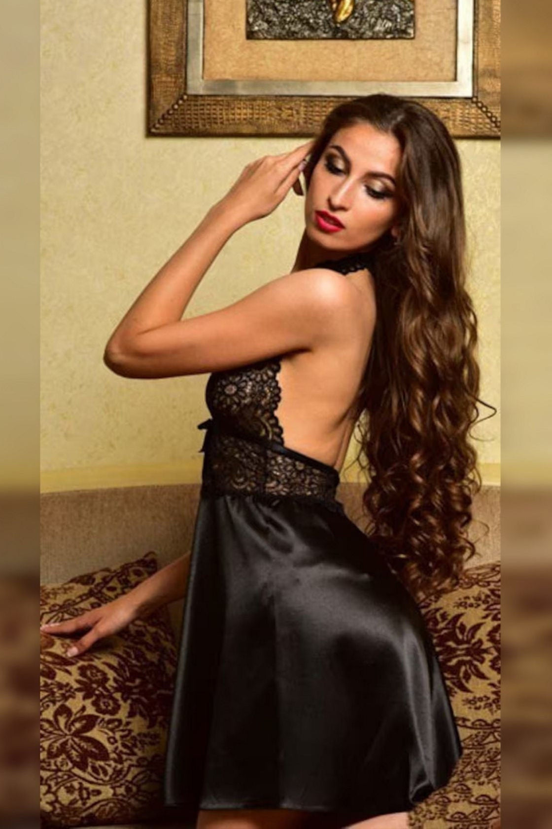 Woman in a black dress posing indoors with a decorative wall in the background