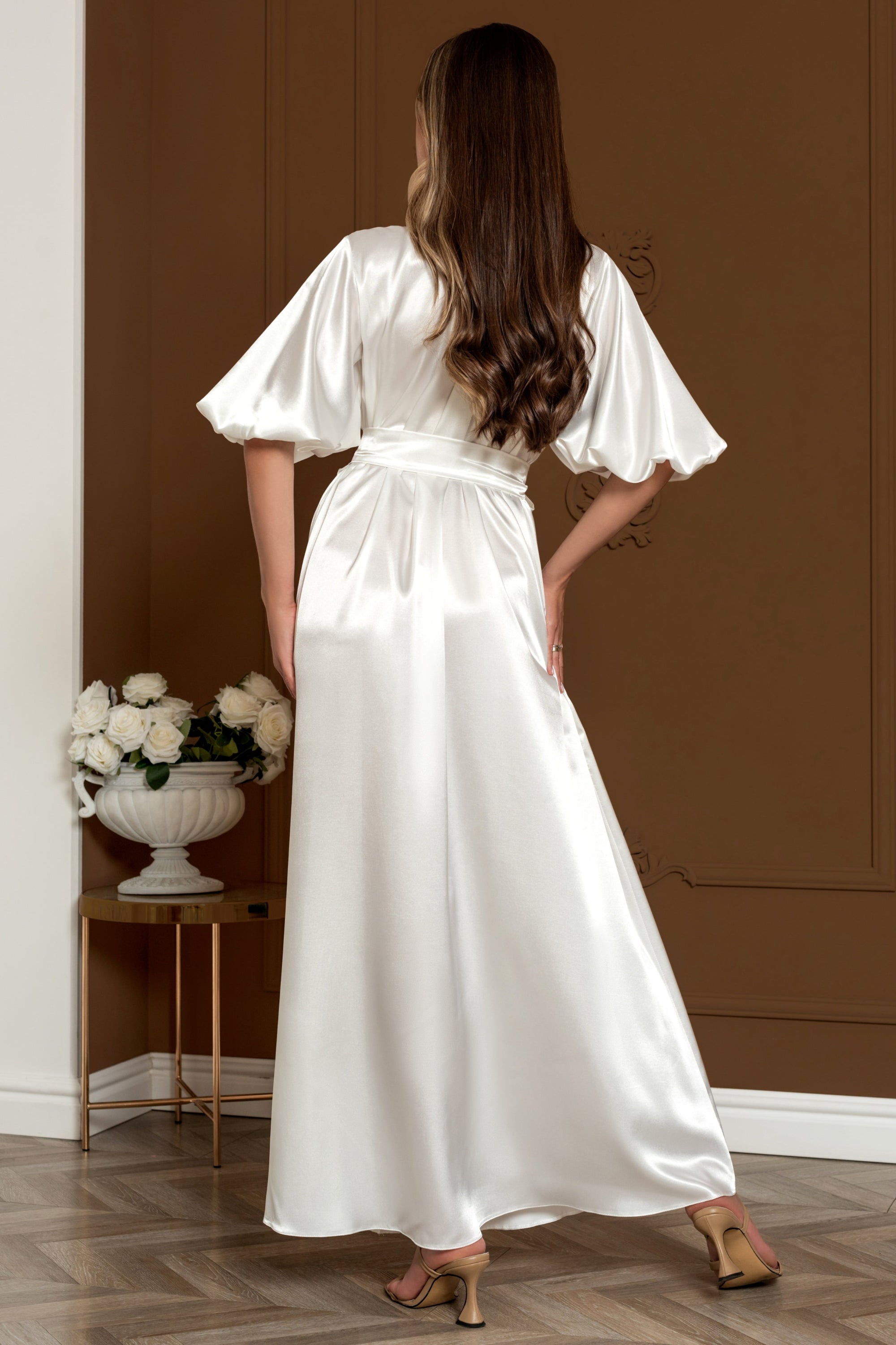 Woman in a dress standing in a room with a brown wall