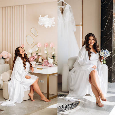 Woman in a white robe sitting on a couch with a wedding dress and bouquet in a stylish room