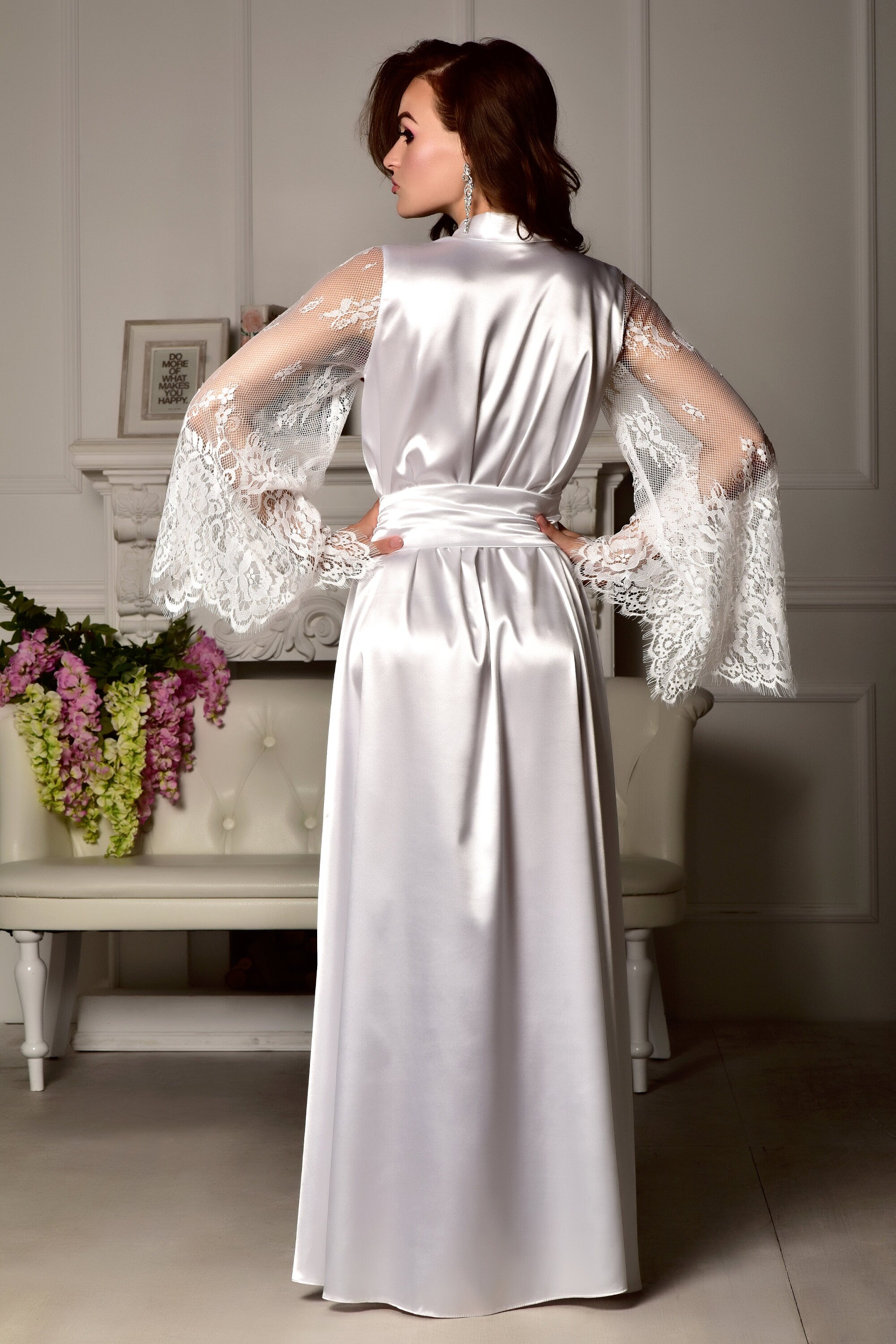 Woman wearing a white satin robe with lace sleeves in a room setting.