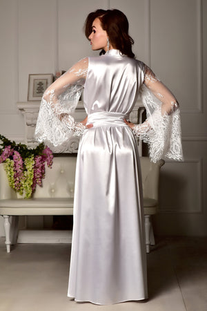 Woman wearing a white satin robe with lace sleeves in a room setting.