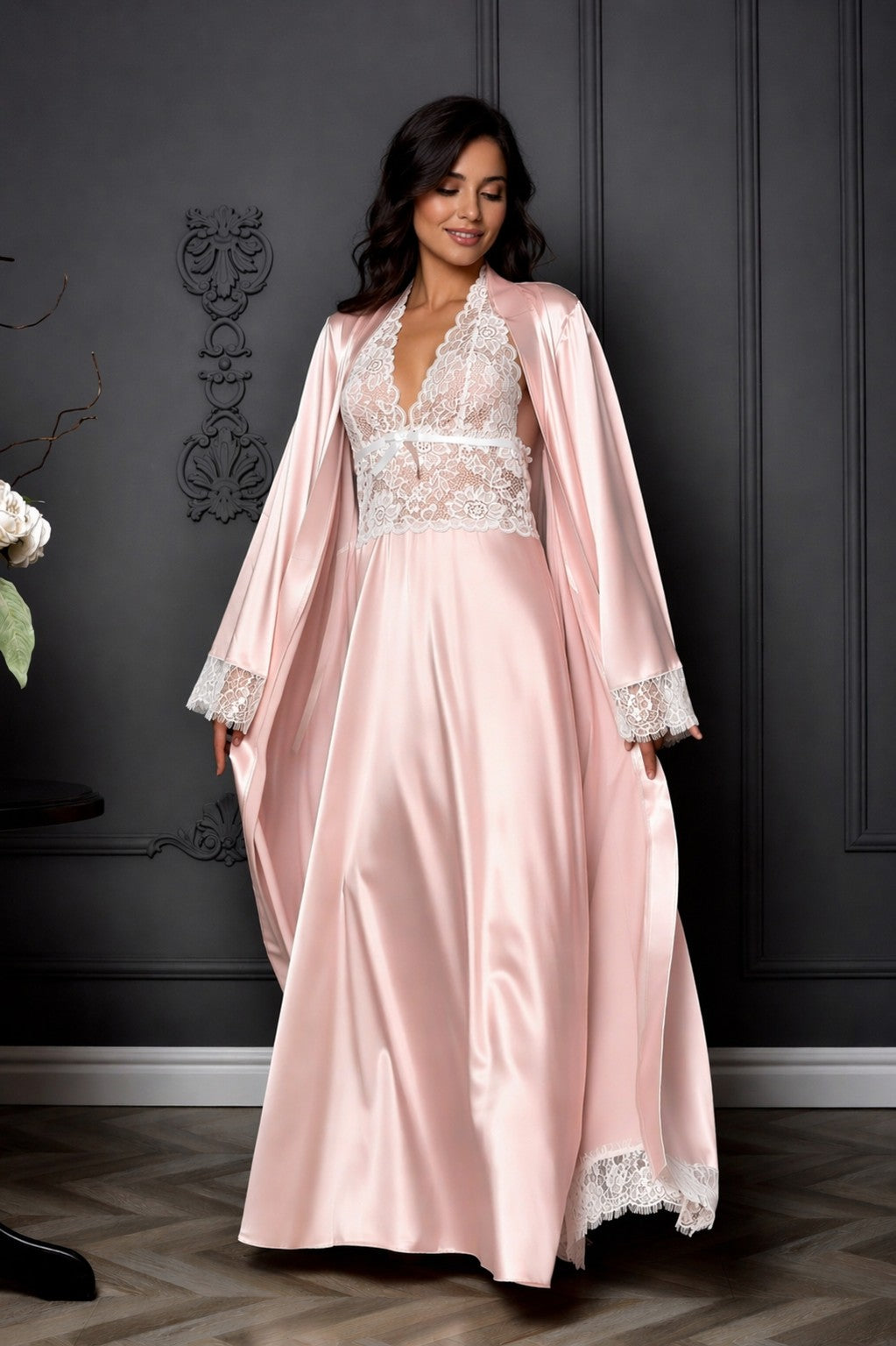 Woman wearing a pink satin robe with lace details against a dark wall.