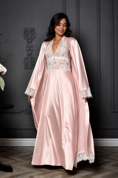 Woman wearing a pink satin robe with lace details against a dark wall.