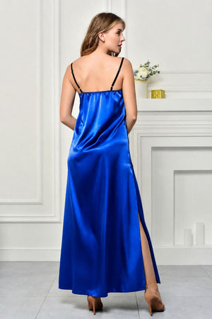 A woman wearing a bright royal blue satin slip dress with thin black straps and a high side slit, photographed from the back in an elegant white room with a fireplace.
