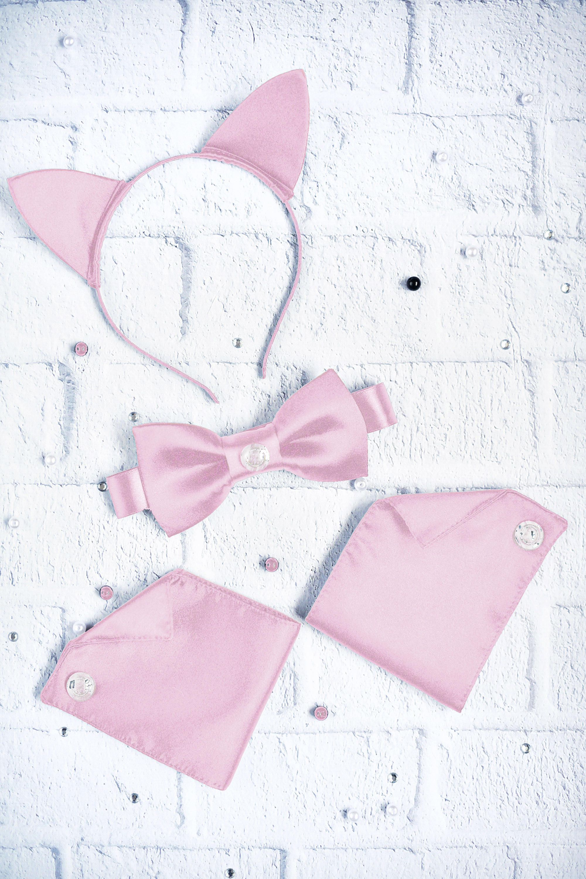 Pink cat ears, bow tie, and tail set on a white brick background