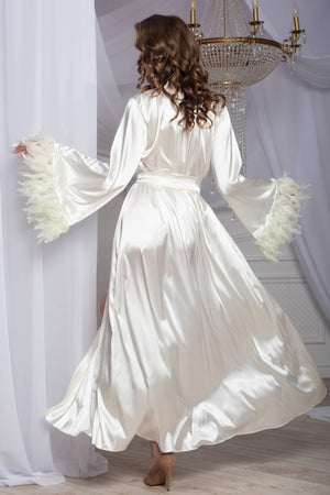 Woman in a white satin robe standing in a room with a chandelier.