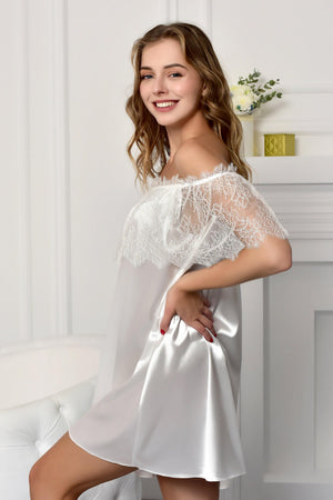 Woman wearing a white lace nightgown in a softly lit room.